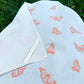 Tea towel with a monarch butterfly pattern, laid flat on grass, with a corner folded over showing the loop on the back corner of the towel. 